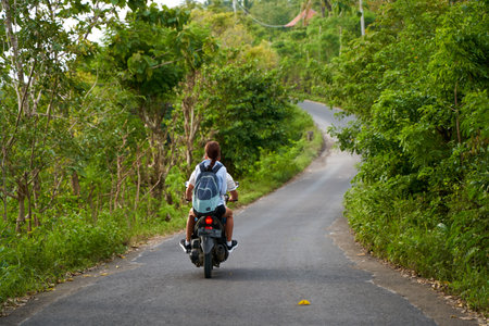 A person on a motorcycle rides a scenic asphalt road in Asia. Bali, Indonesia - 12.30.2022の写真素材