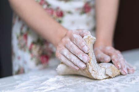 A young girl kneads dough with her hands on the table. High quality photo