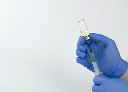 Mens hands in medical gloves hold a syringe inserted into a vial and type the vaccine. High quality...