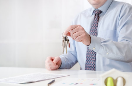 A male realtor holds the keys to the apartment in his hands. There is a contract on the table. High quality photoの写真素材