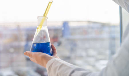 A girl laboratory assistant mixes reagents in flasks in the laboratory by the window. High quality...