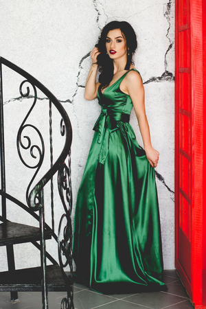 Portrait of brunette with red lips in green dress posing near stepsの写真素材