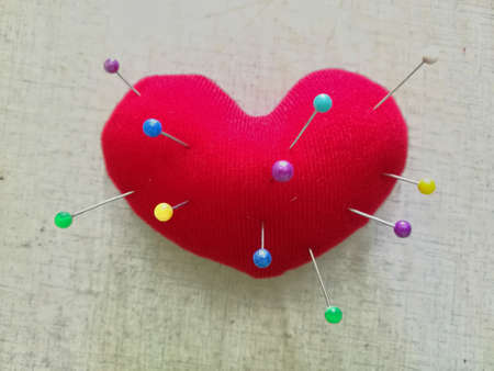 Red heart-shaped pillow with multi-colored pins embroidered on red heart-shaped pillows.