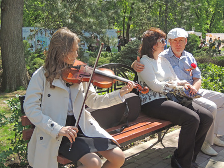 The girl on the bench playing the violin for the townspeople in the public garden on the Victory Dayのeditorial素材