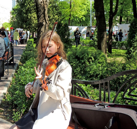 The young adult girl on the bench play the fiddle for free for the city dwellers in the public garden on the Victory Dayのeditorial素材