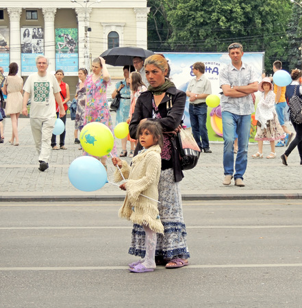 Young women in the dress with frills and jacket with a elementary age girl in knitted dress among city dwellers in the middle of the city square with interest look the Music Festival of Children's Brass Bands in the city central squareのeditorial素材