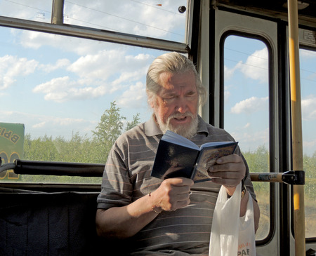Grey-haired  bearded mature men reading a book in the bus in the suburb of Voronezhのeditorial素材