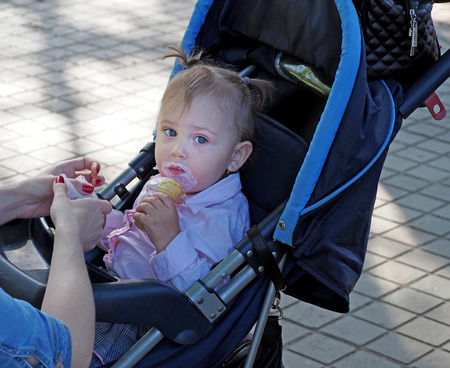 Smeared with ice cream elementary age girl in a pram on a city streetのeditorial素材