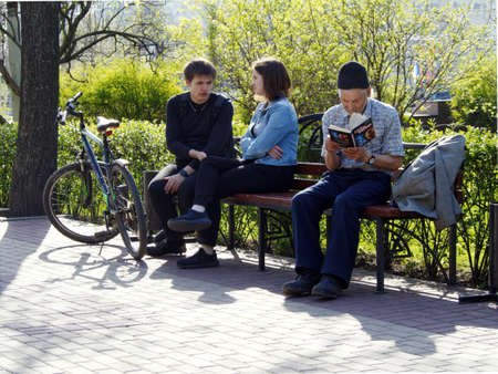 Voronezh, Russia - May 1, 2018: Visitors to the city square relax on a bench. An elderly man reads a book enthusiasticallyのeditorial素材