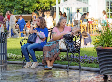 Moscow, Russia - June 19, 2016: An adult chestnut-coloured hair girl and a middle age woman resting on a bench in a city Parkのeditorial素材