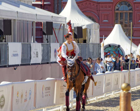 Moscow, Russia - Aug 28, 2016: Adult girl in a Russian national costume doing trick riding on a Bay horse. Festival Spasskaya Towerのeditorial素材
