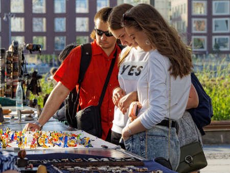 Moscow, Russia - June 2, 2018: Two adult girls and a young man look at glass knick-knack on a street tableのeditorial素材