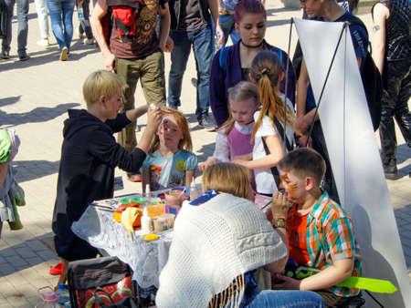 Voronezh, Russia - May 1, 2018: Two young women doing face painting elementary age girl and boy sitting in a chairs on a city streetのeditorial素材