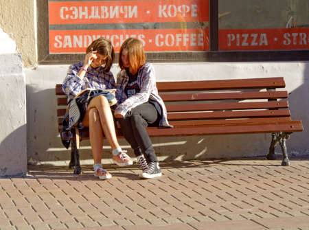 Moscow, Russia, aug 28, 2016: Two girls sitting on a bench look at an open book on the lap of one of themのeditorial素材