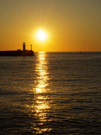 Sunrise over the lighthouse in the sea and patch of sunlight on the water surface