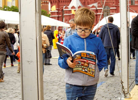 Moscow, Russia - June 4, 2017: Book Festival "Red Square". Standing boy with glasses is reading the open book holding it in your hand.のeditorial素材