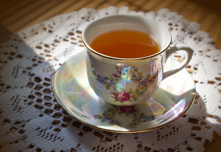 painted china cup of tea with pattern of flowers lying on the white tableclothの写真素材