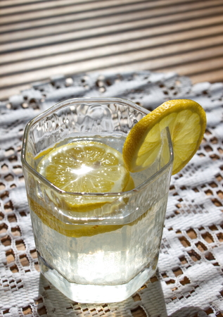 glass of water with pieces of lemon on the tableclothの写真素材