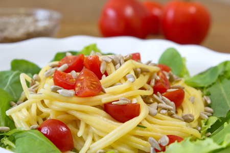 corn spaghetti with tomatoes and sunflower seeds served with saladの写真素材