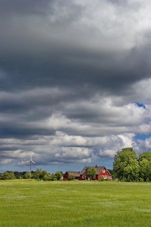estonian countryside - green field, cloudy sky and traditional rural houseの写真素材