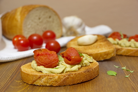 pieces of bread with tomatoes, cream and garlic lying on the rustic tableの写真素材