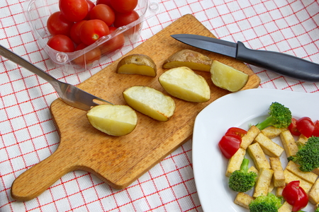 baked potatoes with tofu, broccoli and tomatoes served on checkered tableclothの写真素材