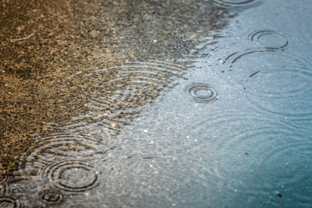 Rain drops rippling in a puddle with blue sky reflection.の写真素材