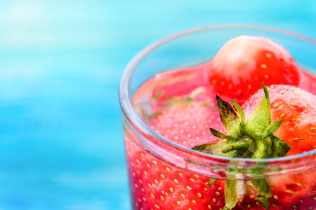 strawberries in a glass of water on a blue wooden backgroundの写真素材