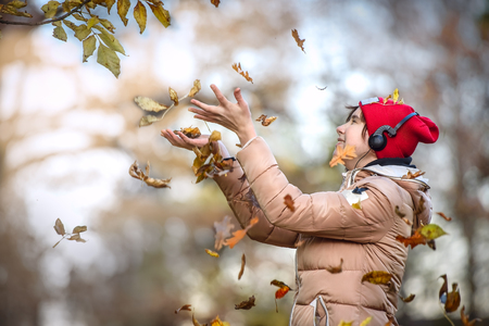 Happy girl with Red cap walks in autumn Park and catches the falling leavesの写真素材