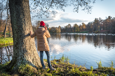 A girl in a red hat wearing headphones enjoys the view of an autumn park. View from the back.の写真素材