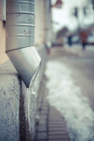 drain pipe on the wall of the house with frozen water along the city sidewalkの写真素材