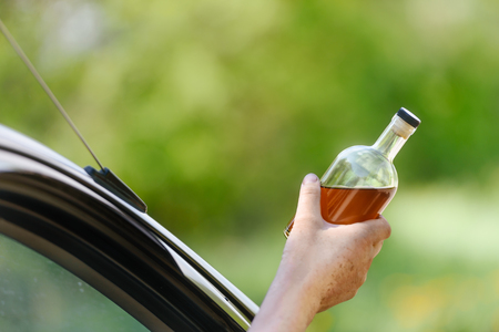 Alcohol, bottle,  car and concept of drunk driving - the person holds in hand a bottle with alcoholic drink, driving the car.の写真素材