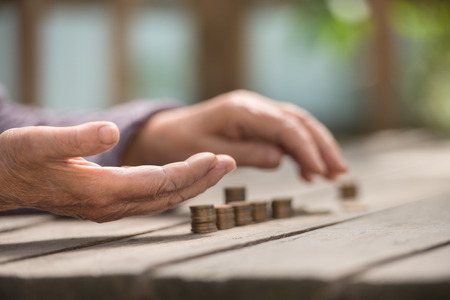 Money, coins, the grandmother on pension and the concept of life, minimum - hands of the old woman recalculate coins on a wooden tableの写真素材
