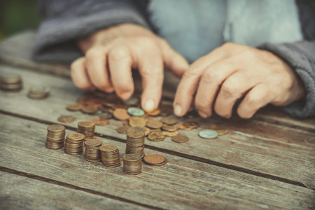 Money, coins, the grandmother on pension and the concept of life, minimum - wrinkled hands of the old woman touch coins on a wooden tableの写真素材