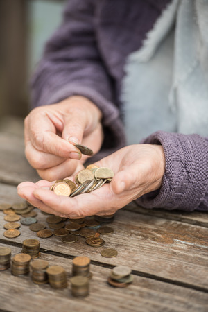 Money, coins, the grandmother on pension and the concept of life, minimum - wrinkled hands of the old woman touch coins on a wooden tableの写真素材