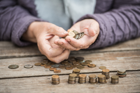 Money, coins, the grandmother on pension and the concept of life, minimum - wrinkled hands of the old woman touch coins on a wooden tableの写真素材