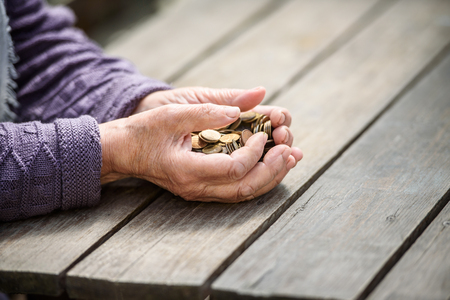 Money, coins, the grandmother on pension and the concept of life, minimum - hands of the old woman to hold a handful of coins on a wooden tableの写真素材