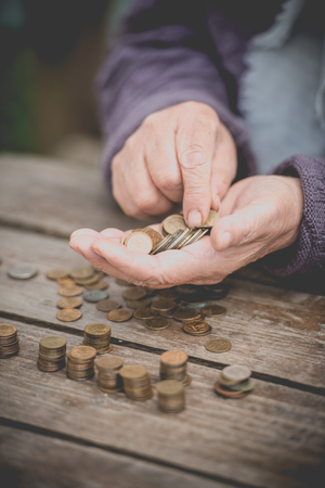 Money, coins, the grandmother on pension and the concept of life, minimum - wrinkled hands of the old woman touch coins on a wooden tableの写真素材