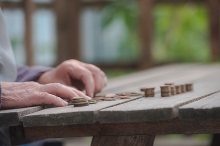 Money, coins, the grandmother on pension and the concept of life, minimum - wrinkled hands of the old woman touch coins on a wooden tableの写真素材