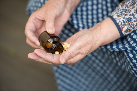 Pills, old age and health concept - pills in the hands of an old lady closeupの写真素材