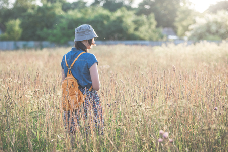 A girl in a dress and hat is walking in the field at sunset. The concept of outdoor recreation.の写真素材