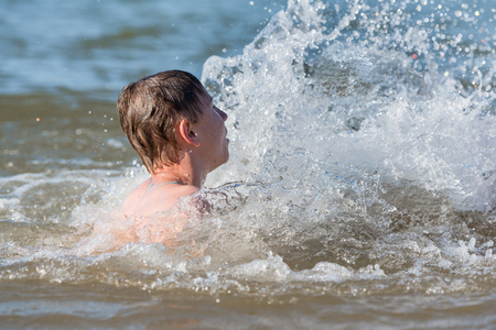 A boy teen swims in a spray of water - a concept of a beach holidayの写真素材