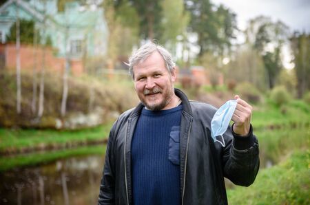 A happy middle-aged man removes a medical mask from his face in a spring Park. Over the coronavirus. End of the pandemic, epidemic, and quarantine. の写真素材