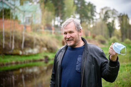 A happy middle-aged man removes a medical mask from his face in a spring Park. Over the coronavirus. End of the pandemic, epidemic, and quarantine. の写真素材