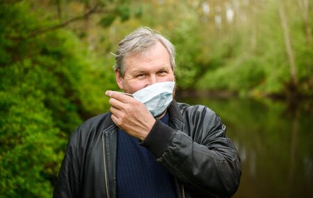 A happy man on a nature walk by the river in a medical mask rejoices at the end of the quarantine.の写真素材