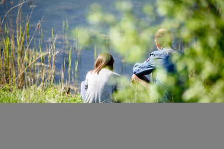  couple relaxing on the lake-view from behind green trees in soft focusの写真素材