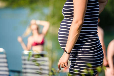 Pregnant woman in a striped dress on the beach. Belly close-up.の写真素材