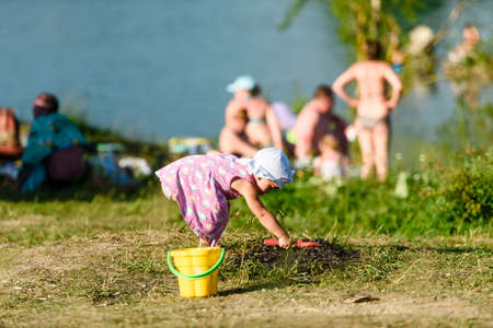 Russia, Saint Petersburg, June 24, 2020: a Little girl in a pink dress plays in the sand on the shore of a lakeのeditorial素材
