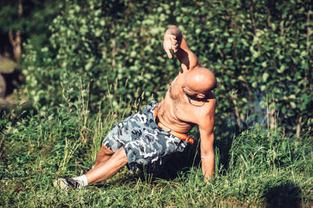 Russia, Saint Petersburg, June 24, 2020: a Muscular man with a naked torso does sports in nature in the summerのeditorial素材