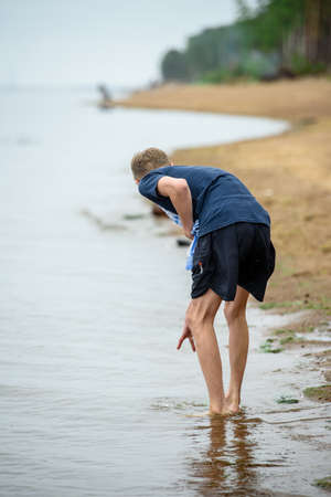 tall boy on the beach is standing with his feet in the waterの写真素材